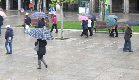 Los pamploneses pasean por la Plaza del Castillos bajo sus paraguas.