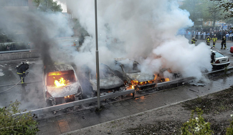 Bomberos extinguen el fuego en un carro incendiado despu&eacute;s de disturbios, originados por j&oacute;venes en diferentes suburbios alrededor de Estocolmo