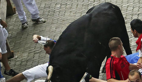 Uno de los toros de la ganadería de Victoriano del Río Cortés cornea al mozo de Chicago en el tercer encierro de los Sanfermines. efe