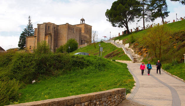 Paseantes camino del puente sobre el río Irati. Arriba, la iglesia que 'flanquean' dos árboles singulares.
