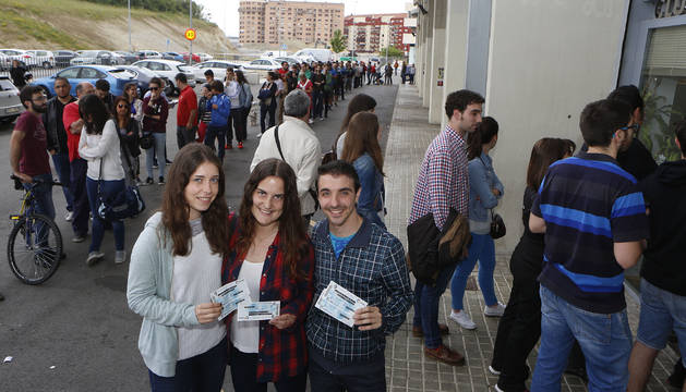 Tres aficionados rojillos posan orgullosos con sus entradas mientras cientos de personas hacen cola a sus espaldas para adquirir una.