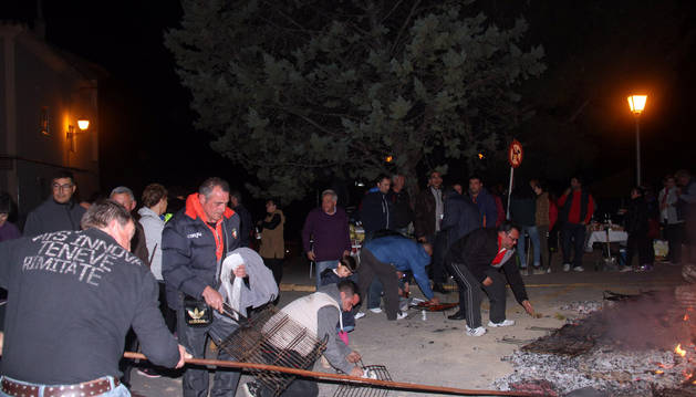 Varios vecinos asan distintos alimentos sobre las brasas de la hoguera con motivo de la fiesta de San Martín.