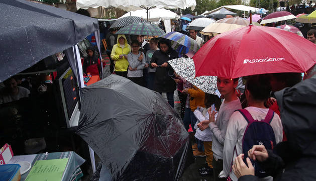 Los vecinos curiosean los puestos de artesanía mientras se resguardan de la lluvia bajo los paraguas.
