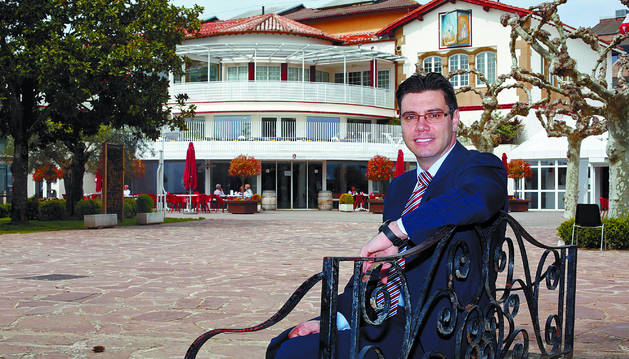 Alejandro N. García Martínez, actual presidente del Club de Tenis de Pamplona, posa en un banco frente al edificio social del de club, con el tejado del trinquete al fondo.