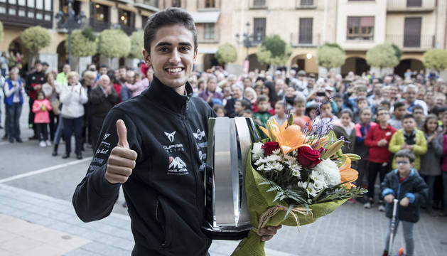 Pulgar en alto de Mikel Azcona, con la plaza del Ayuntamiento de Falces detrás. El navarro sujeta en su mano izquierda el trofeo de campeón de Europa y un ramo de flores.