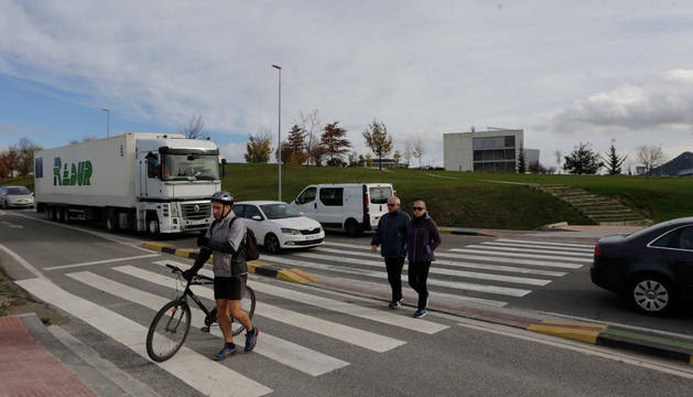 Un ciclista con la bici en la mano y dos peatones más cruzan por el paso de la carretera NA-2300 entre la rotonda de Sarriguren y el polígono Areta para llegar desde la Ciudad de la Innovación a Erripagaña.