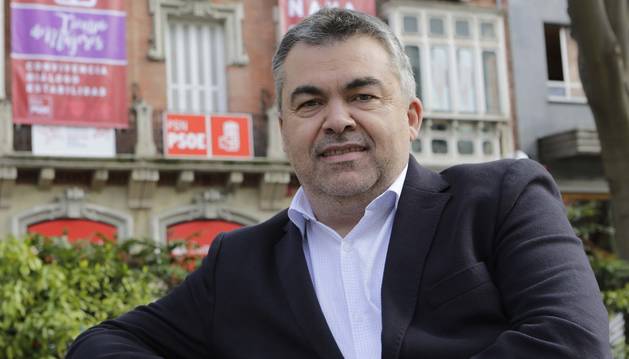 Santos Cerdán, sentado en un banco del Paseo de Sarasate. Tras él, el edificio donde está la sede del PSN, con sus carteles de campaña.