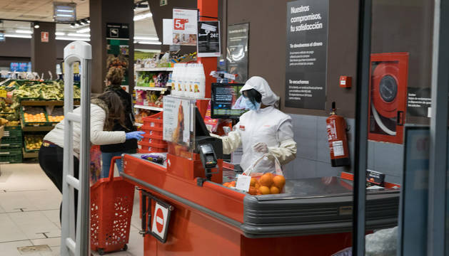 Imagen de un supermercado Eroski. La dependienta, con mascarilla, y la clienta, con guantes.
