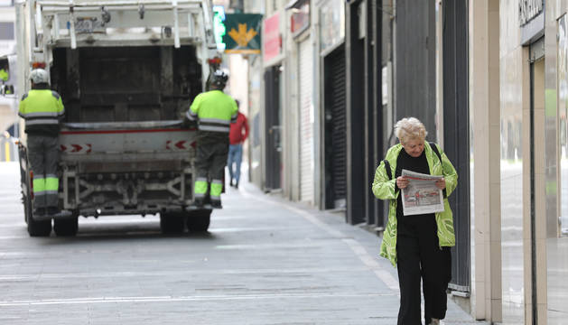 Una mujer regresa de comprar el pan y la prensa en Pamplona. Al fondo, el servicio de recogida de basuras, que sigue funcionando.