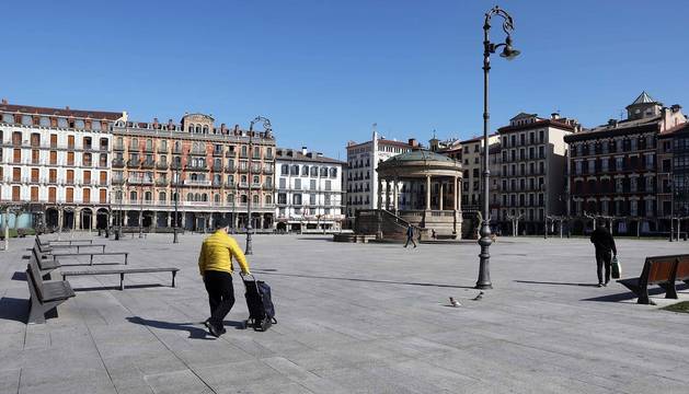 Una persona con un carro de la compra pasa por una vacía Plaza del Castillo de Pamplona.