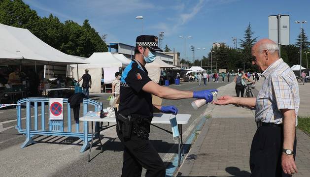 Un agente proporciona gel desinfectante y mascarilla a una persona en el acceso al mercadillo.