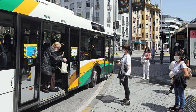 Varias personas cubiertas con mascarillas esperan para subir a la villavesa en una parada de la Plaza de Merindades de Pamplona.