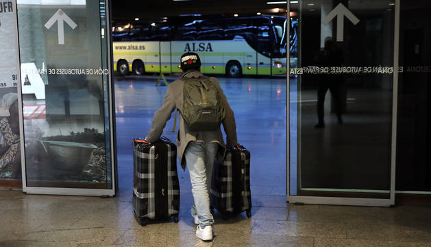 Un hombre se dirige con dos maletas a coger un autobús en la estación de Pamplona.