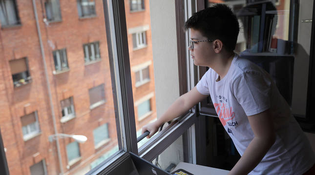 Un niño de 11 años mira a lo lejos por la ventana, después de consultar el ordenador.