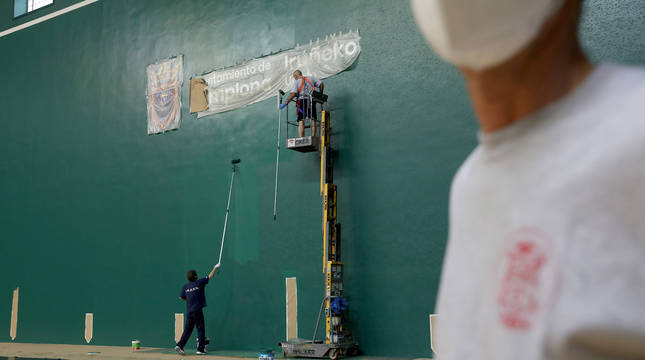 Dos operarios de la Federación Navarra de Pelota pintan la pared izquierda del Labrit este lunes por la mañana.