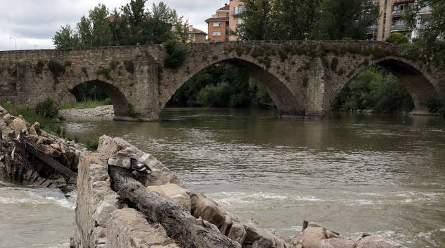 La presa de Santa Engracia con la escotadura central por donde se cuela el agua del río Arga desde hace más de dos años. Al fondo, el puente de Santa Engracia.