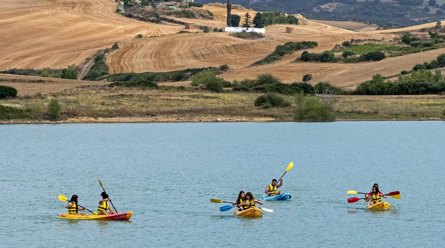 Alumnos de la escuela practican piragüismo en el embalse de Alloz con Villanueva de Yerri de fondo