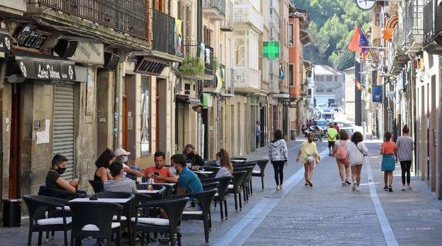 Varias personas toman algo en cafeterías y otras pasean en la calle Mayor de Sangüesa.