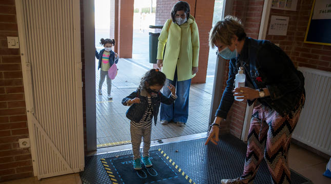 Daniela, de 4 años, desinfecta sus zapatos tras soltar a su madre, con abrigo amarillo, Marta Sampedro.