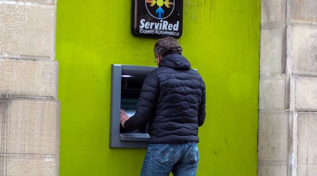 Foto de un hombre sacando dinero en una cajero.