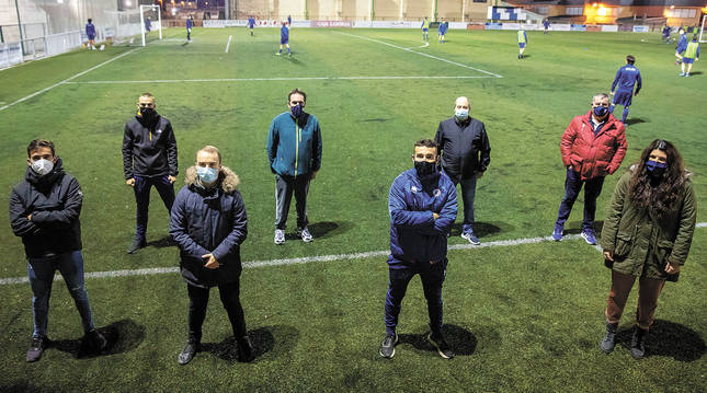 Los miembros de la junta directiva de la Unión Deportiva Mutilvera, en el campo de Mutilva, mientras al fondo entrena un equipo.
