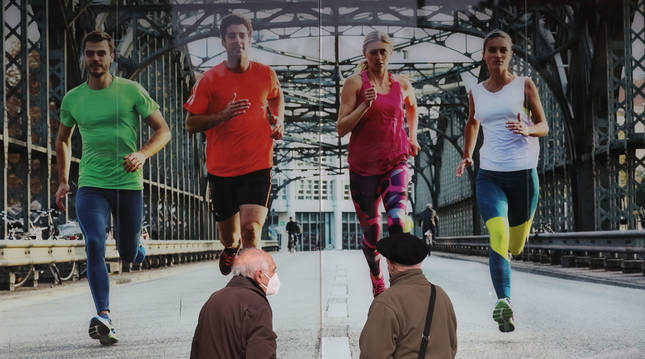 Foto de dos personas mayores se detienen a mirar un mural de publicidad en una calle de Pamplona.