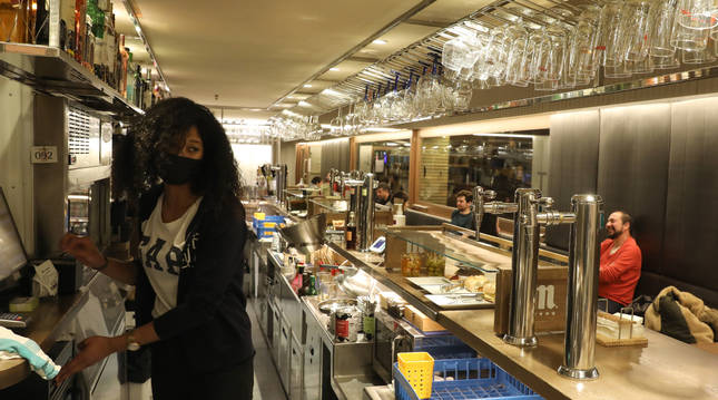 Foto de una trabajadora de El Tinglado, en Pamplona, con clientes en las mesas del local esta semana, antes del cierre de los interiores.
