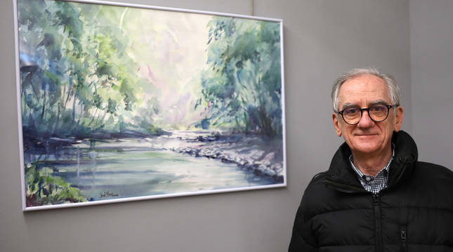 Miguel Oliver Ferrer junto a una de sus obras de la exposición Acuarelas. Se trata de un paisaje abierto realizado con pincel y trazos gordos.