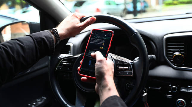 Un conductor lee y escribe mensajes en su teléfono, mientras sostiene el volante de su vehículo.