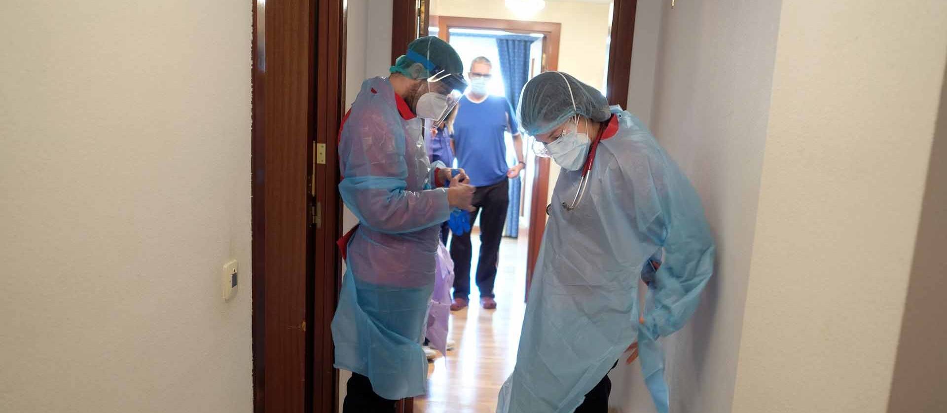 Foto de María Hidalgo, internista, y David García, enfermero, se preparan en el rellano de la casa de un paciente con covid antes de entrar.